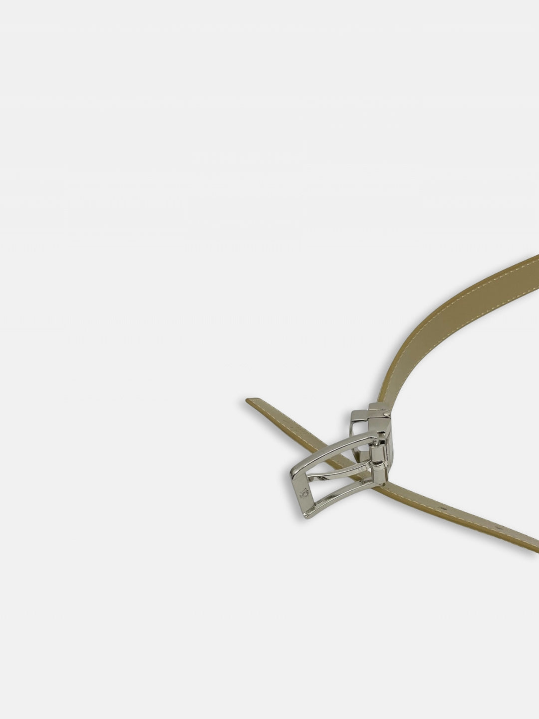 Ceinture fine en cuir beige doré avec boucle à ardillon chromée dissimulant deux petits strass de chaque coté de l'ardillon. Sur fond gros clair. Vue boucle et bout